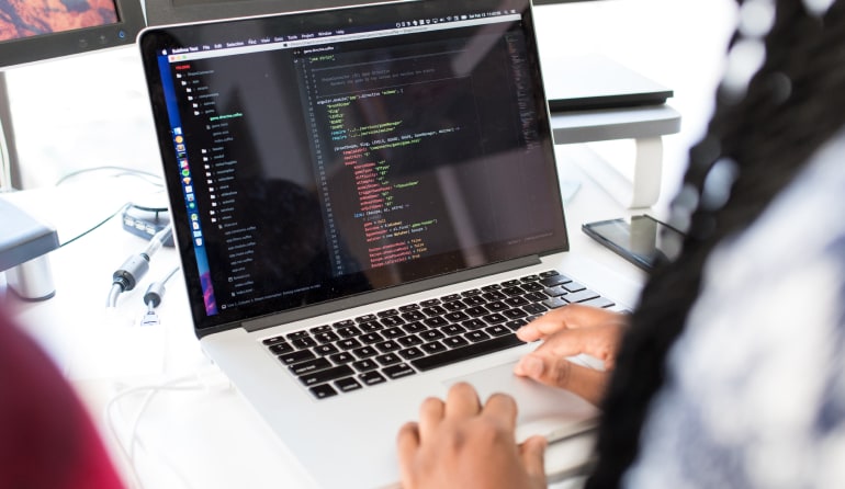 A woman from behind coding on a laptop.